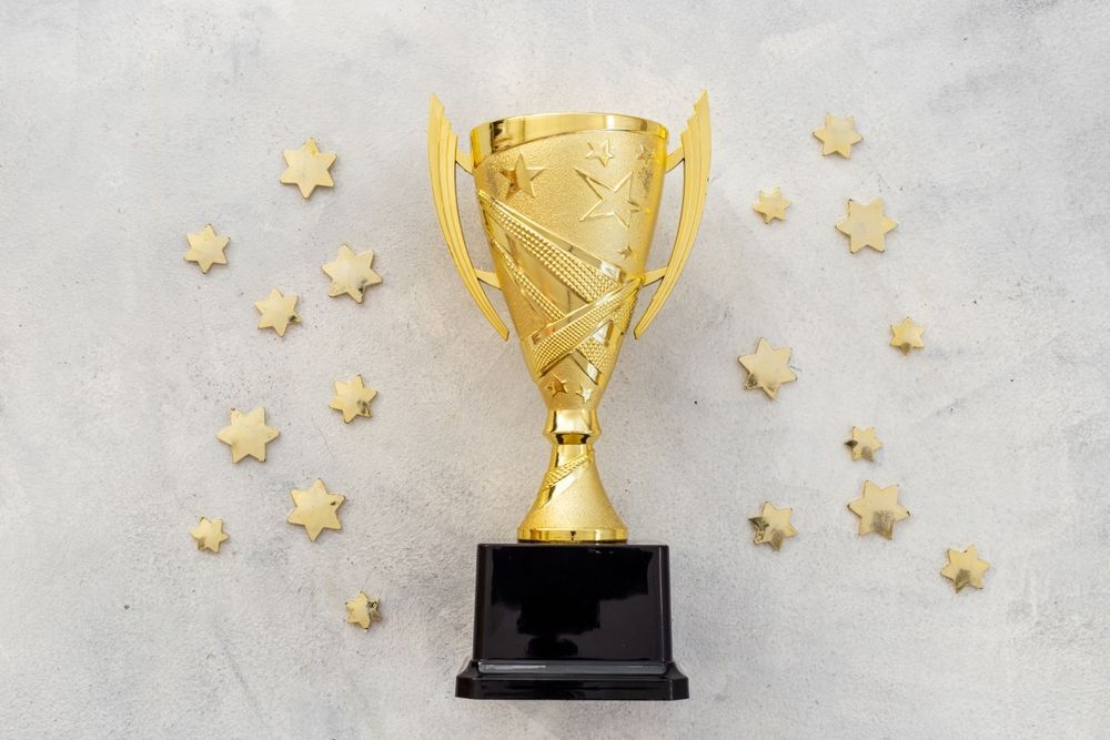A gold trophy is surrounded by gold stars on a white surface.