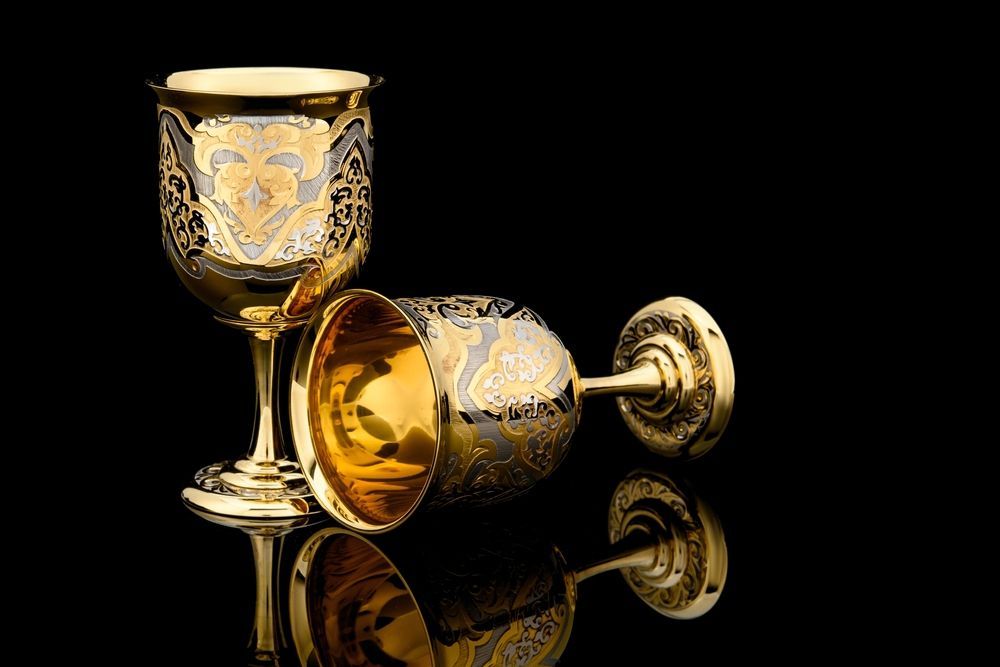 Two gold wine glasses are sitting on a black surface.