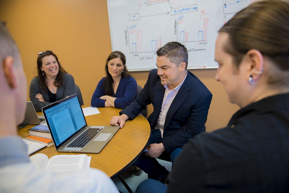 A group of people are sitting around a table looking at a laptop.
