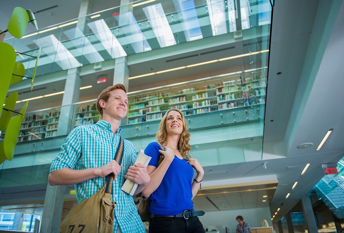 A man and a woman are standing in a library looking up at the ceiling.