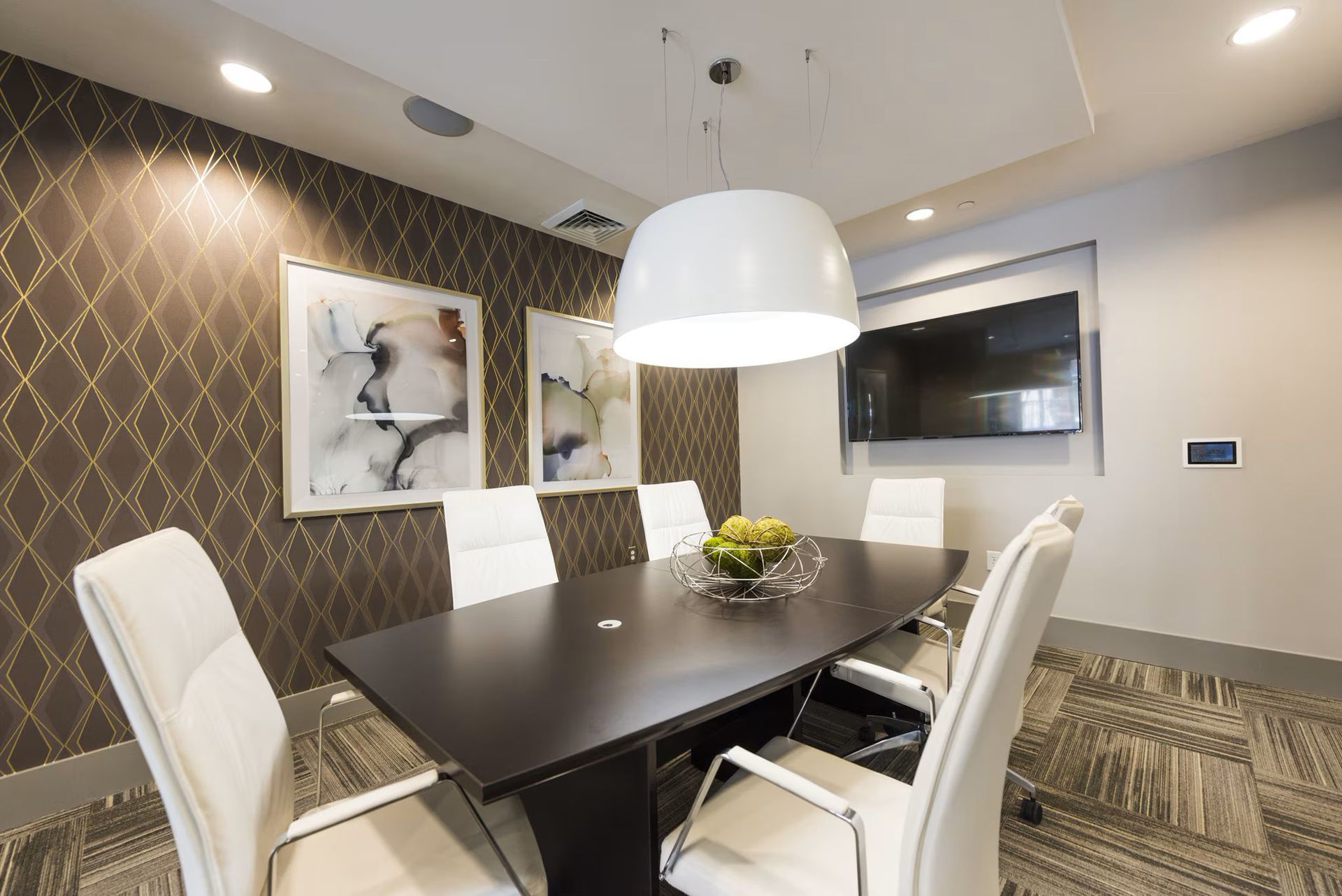 Meeting room with dark table, white chairs, art, TV, and decorative wallpaper.