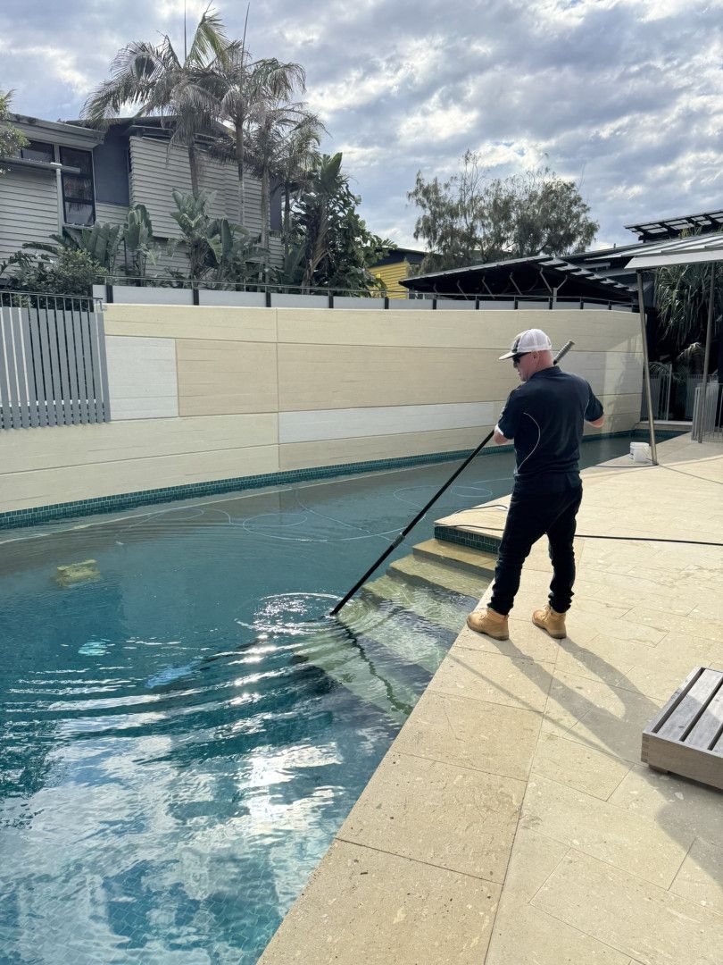 A Man Is Cleaning a Swimming Pool with A Broom — Poolside Noosa in Noosaville, QLD