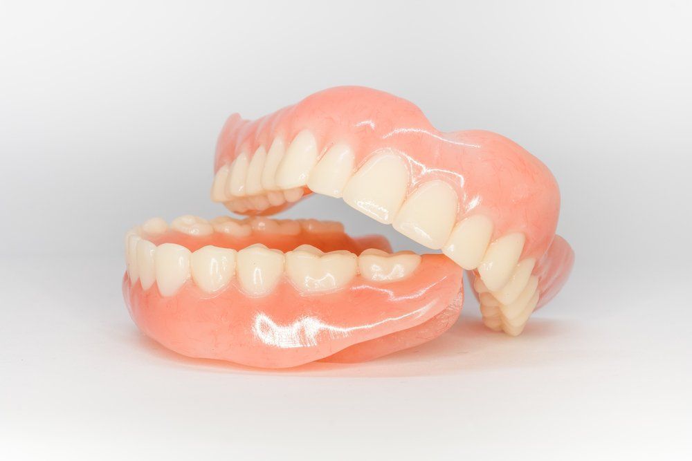 A set of upper and lower dentures, white teeth in pink gum-like bases, against a white background.