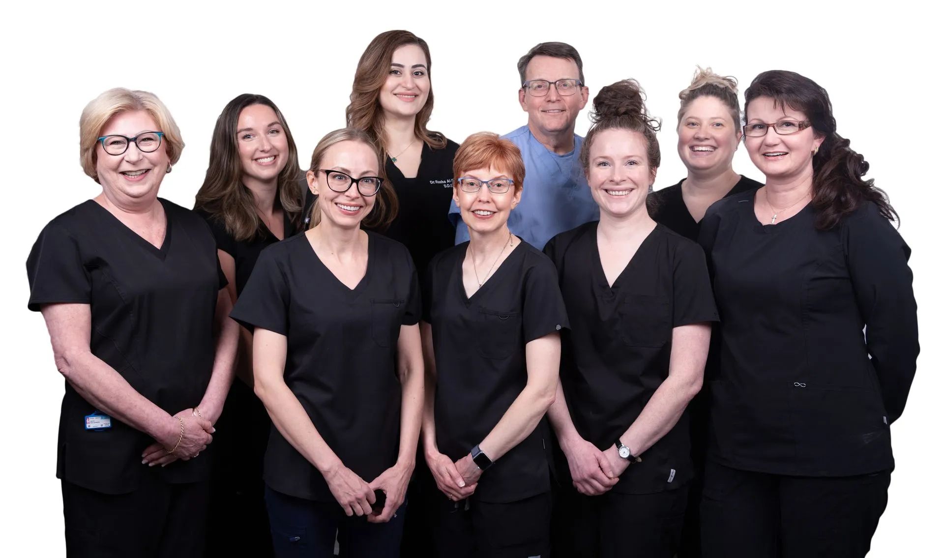 Group of dental professionals in black scrubs, smiling, posing together indoors.