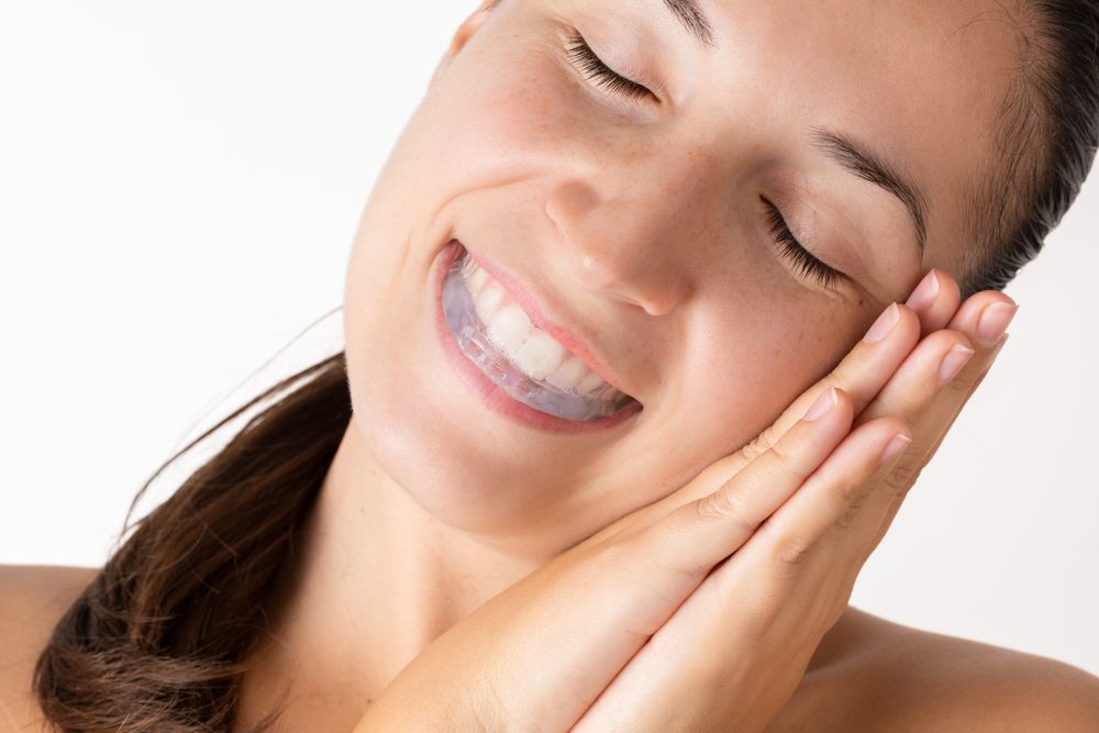 Woman with eyes closed and a teeth whitening tray in her mouth, smiling.