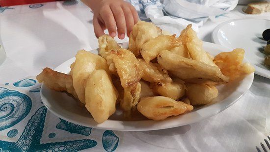Un piatto di pasticcini dorati fritti su un tavolo, con una mano che si protende verso di essi.