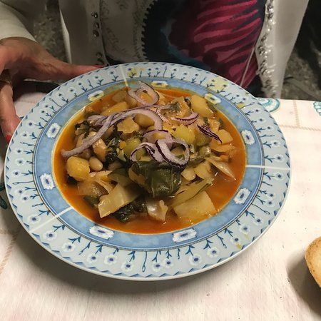 Piatto di cibo messicano in salsa rossa, guarnito con cipolle a fette ed erbe aromatiche su un piatto decorato.