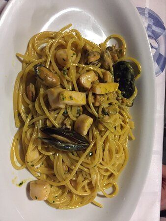 Spaghetti con frutti di mare ed erbe aromatiche serviti su un piatto rettangolare bianco.