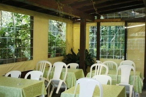 Zona pranzo all'aperto con sedie di plastica bianca e tovaglie verdi sotto un patio coperto.