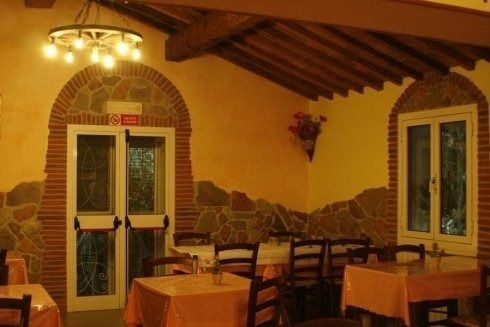Interno rustico di un ristorante con soffitto in legno, pareti in pietra e tavoli apparecchiati con tovaglie rosse.
