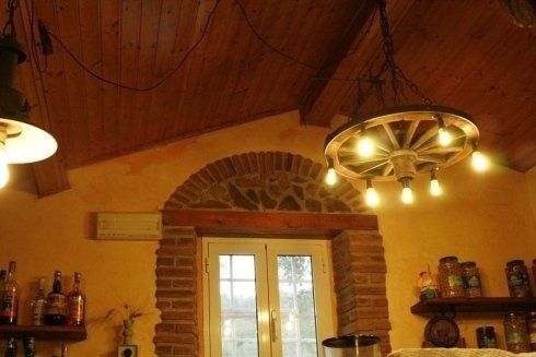 Accogliente stanza in stile rustico con soffitto a volta rivestito in legno, porta in mattoni e lampade circolari a sospensione.