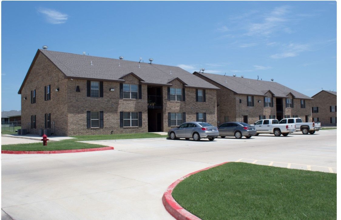 Brick apartment building with parked cars and a curved driveway under a clear blue sky