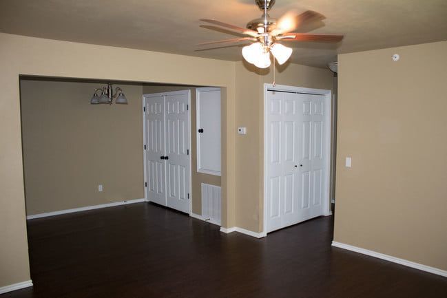 Empty beige room with dark wood floor, ceiling fan, and white double doors