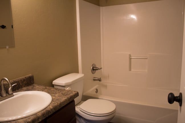Small bathroom with a sink, toilet, and white bathtub/shower surround with grab bar.