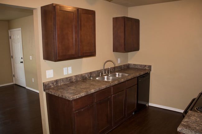 Empty kitchen wet bar with dark wood cabinets, granite countertop, and sink against beige walls