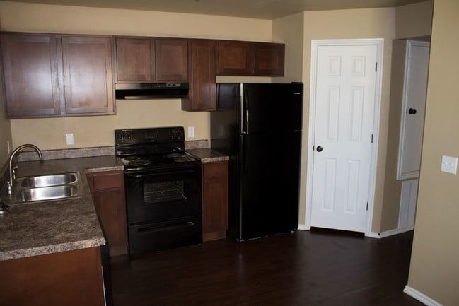 Small kitchen with brown cabinets, black appliances, countertop, sink, and white pantry door.