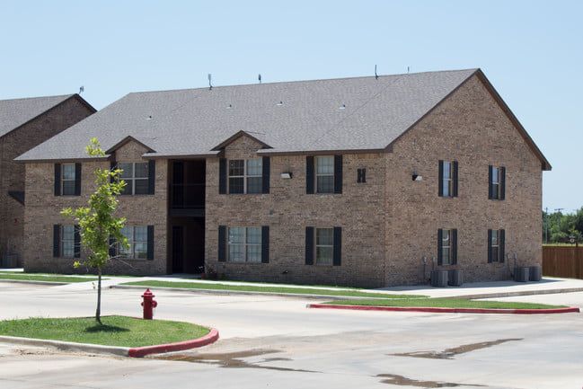 Two-story brick apartment building with a central entrance and parking lot in front