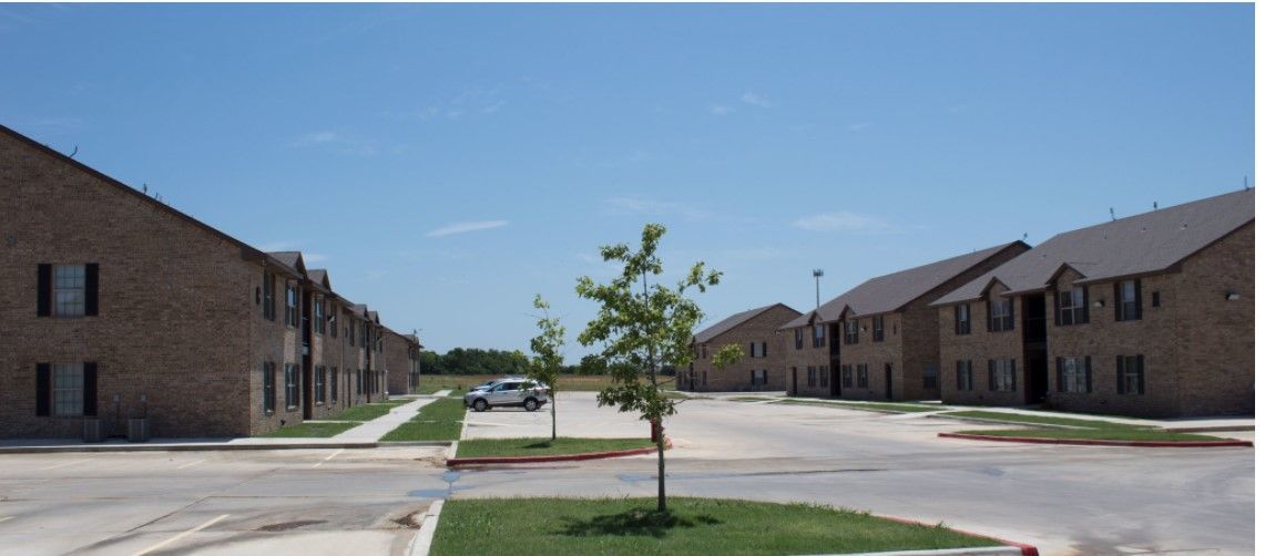 Apartment complex courtyard with a small tree, parked car, and brick buildings on both sides