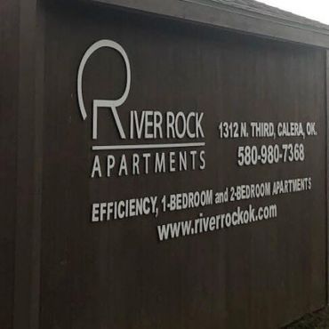 River Rock Apartments sign on a dark wall, with address, phone number, and website.