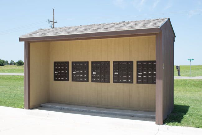 Small brown roadside mailbox shelter with multiple black mailboxes on a grassy field background