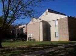 Apartment building with beige siding and brick walls under a clear blue sky, viewed from a grassy yard.