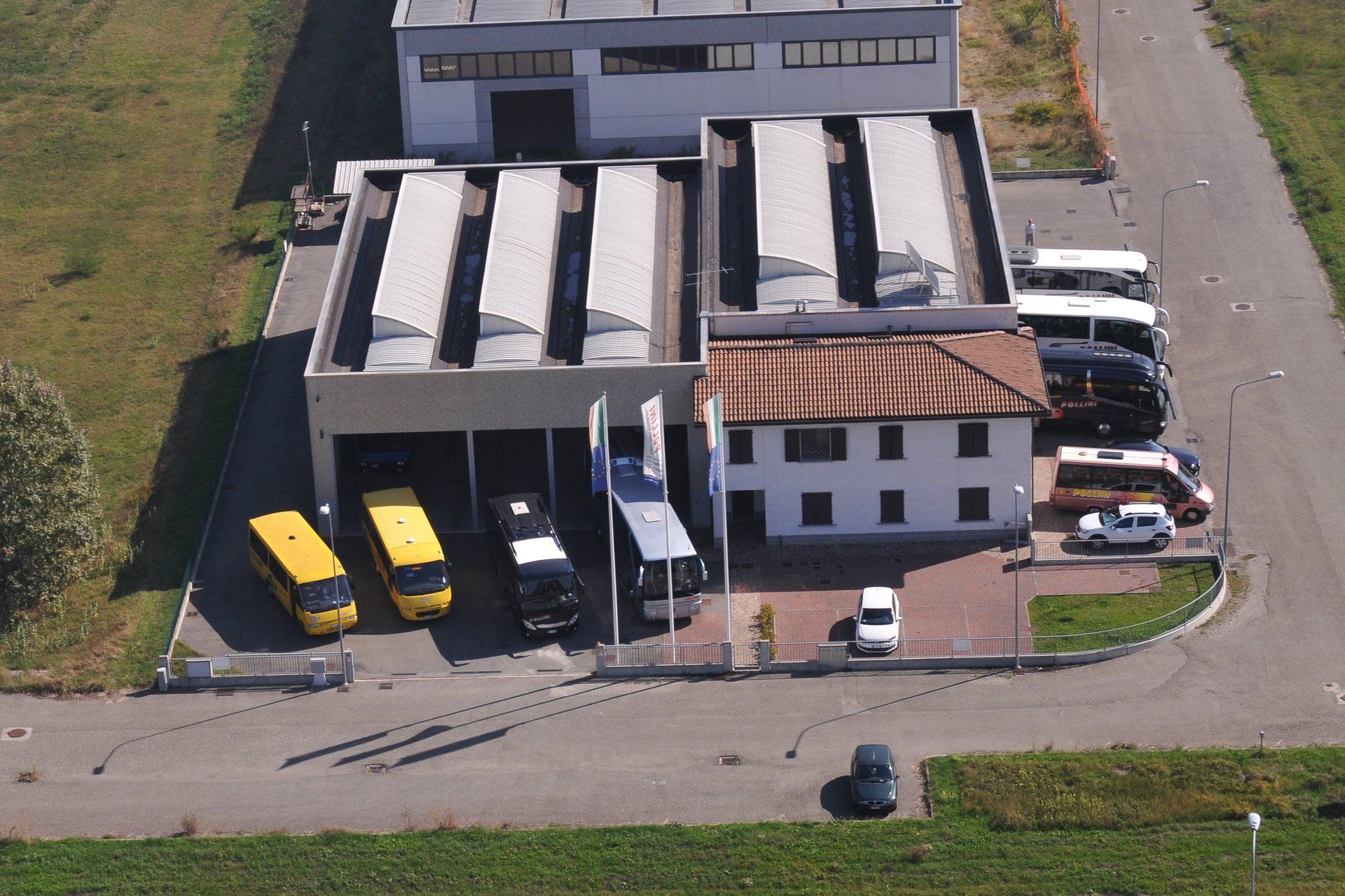 Aerial view of a building complex with buses parked outside. Yellow and silver buses under the shelters.