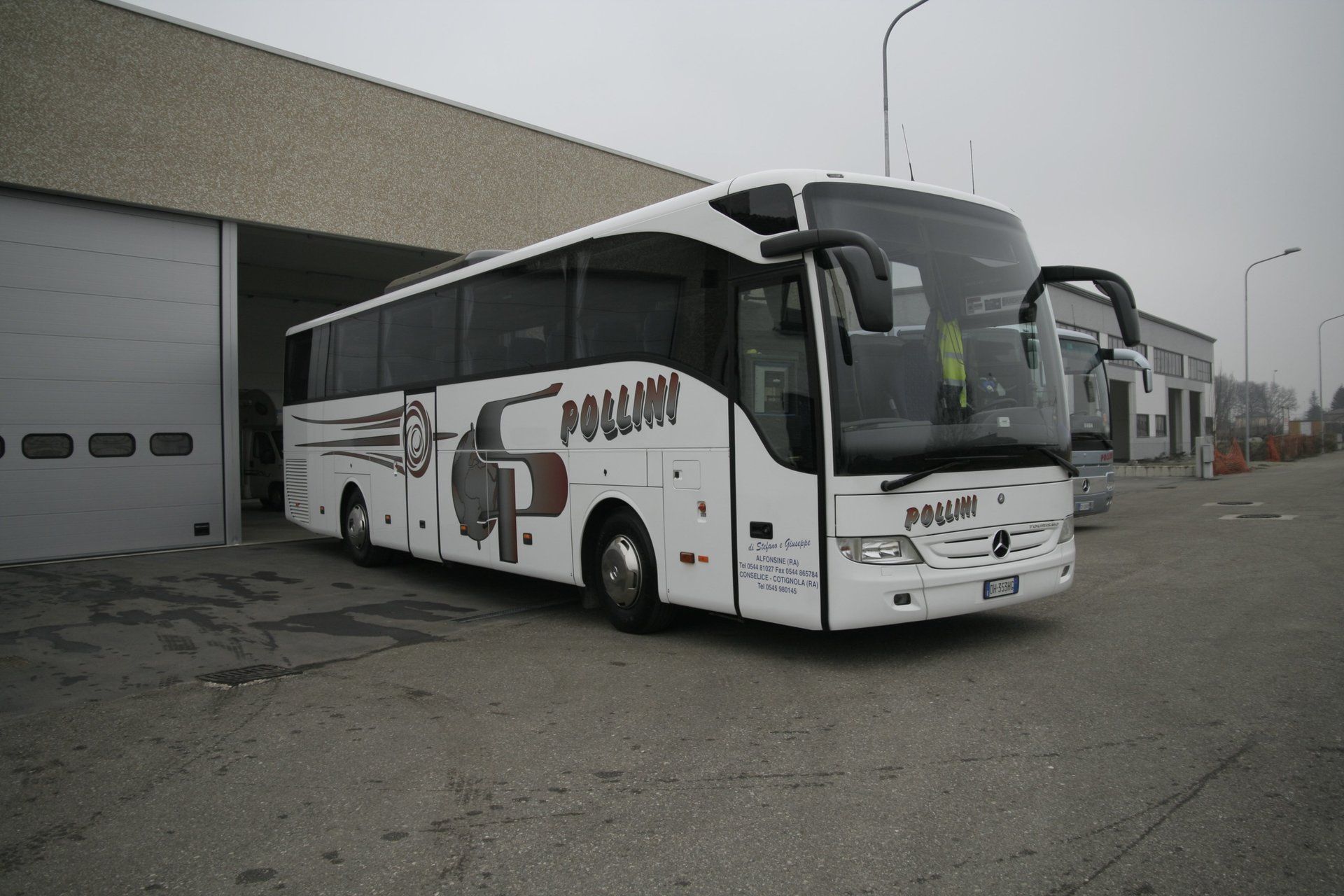 A white bus parked in front of a building with a large garage door. The bus has the word