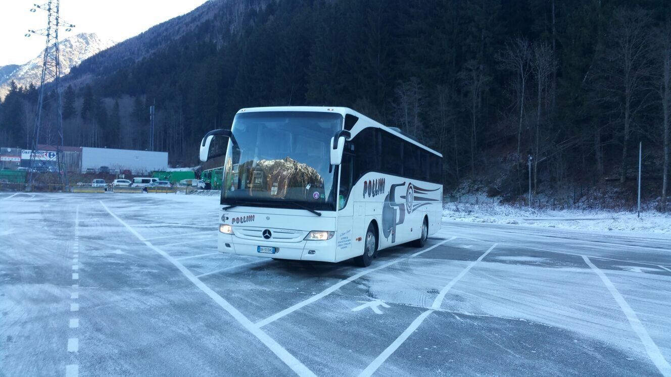 White bus in a snow-covered car park, with trees and mountains in the background.