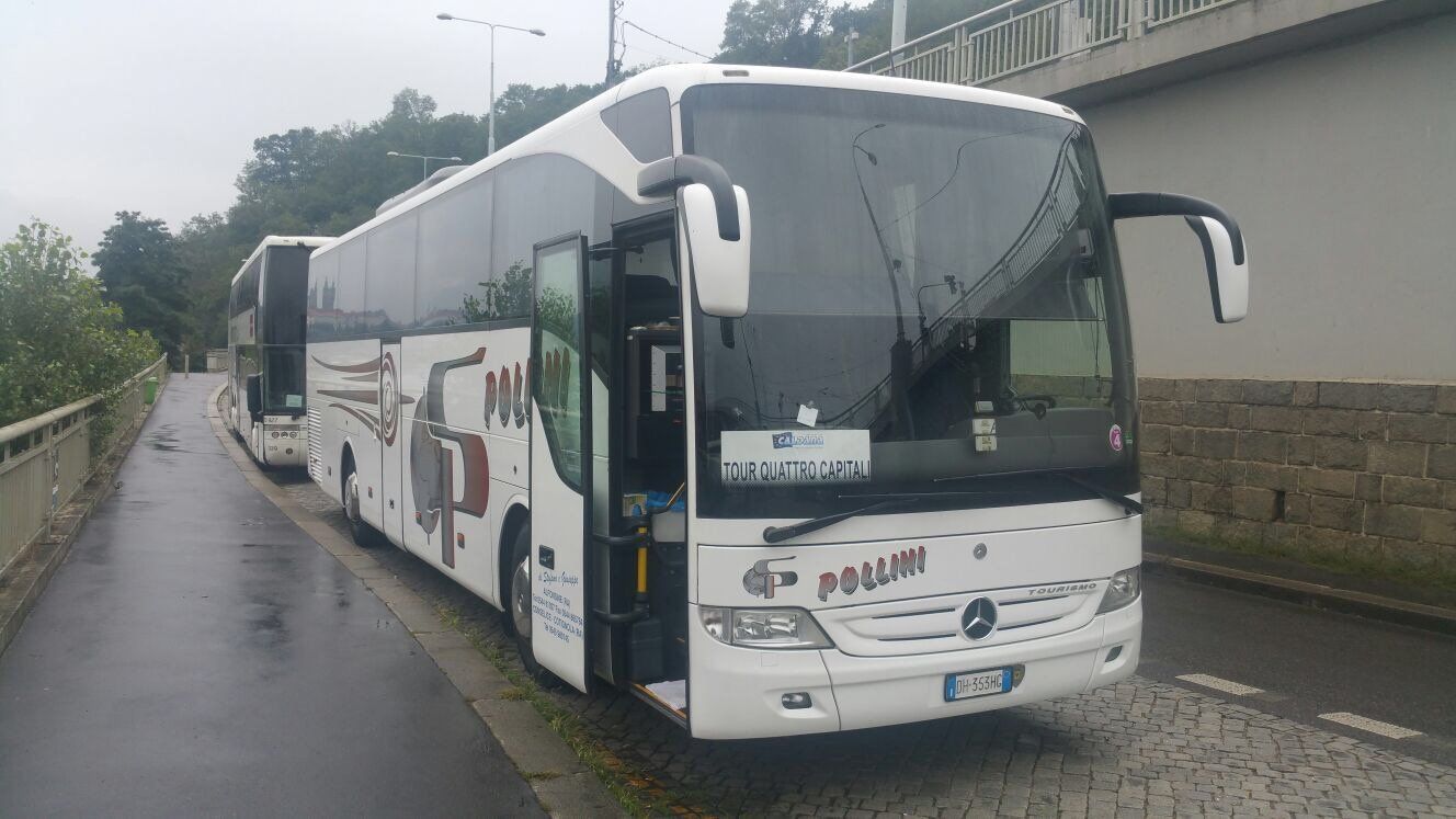 Two white buses parked on a wet road. One of the buses has its door open.