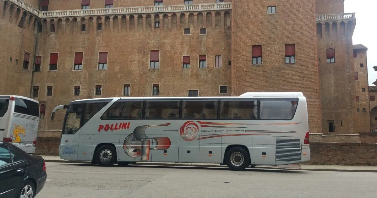 A silver tourist bus parked in front of a large brick castle.