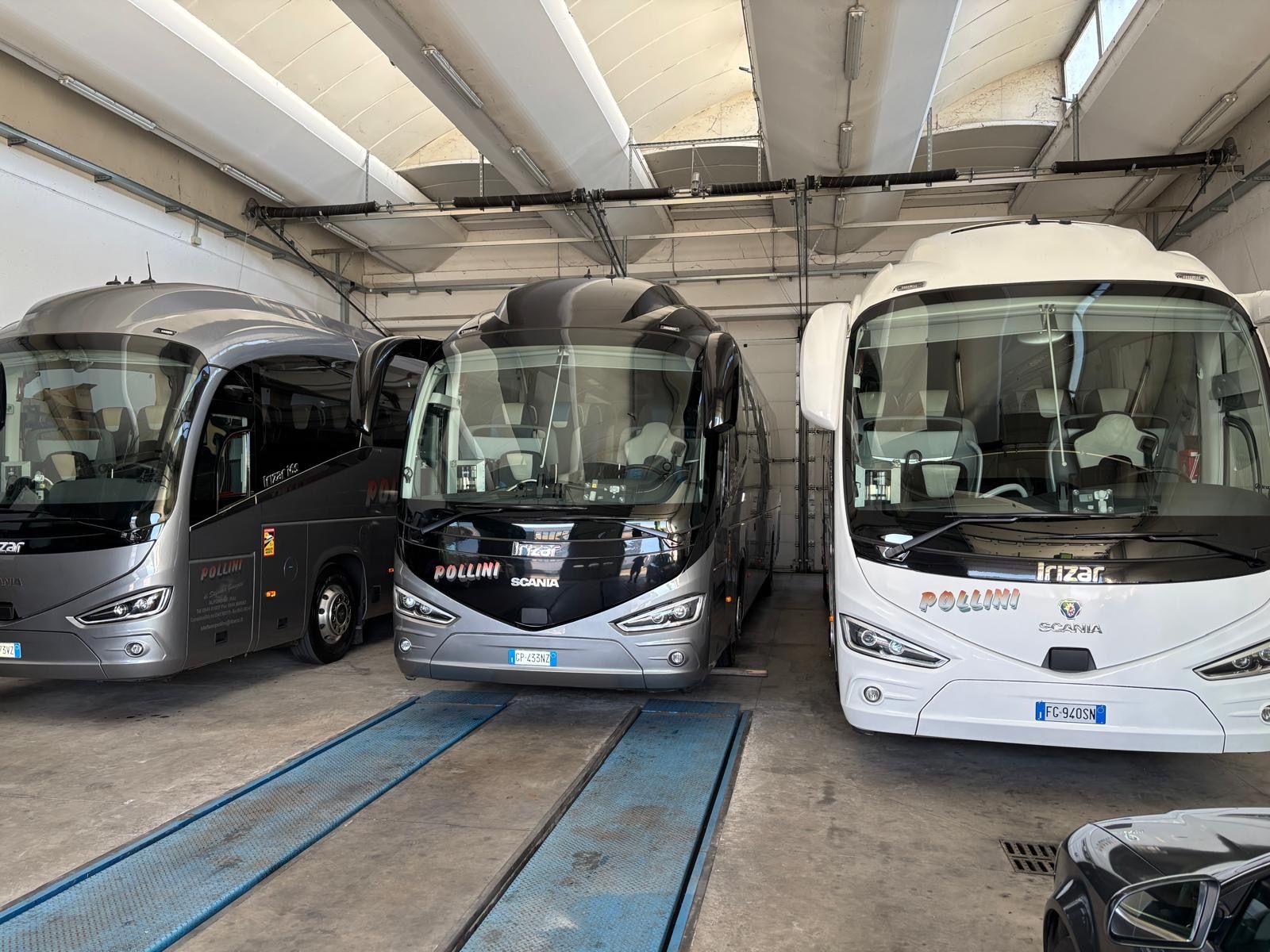 Three white buses parked under a covered structure. 