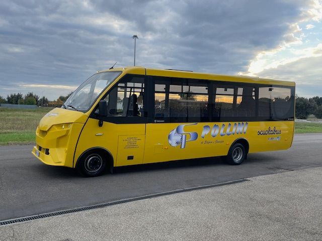Yellow bus parked on a paved surface with a logo on the side, under a cloudy sky.
