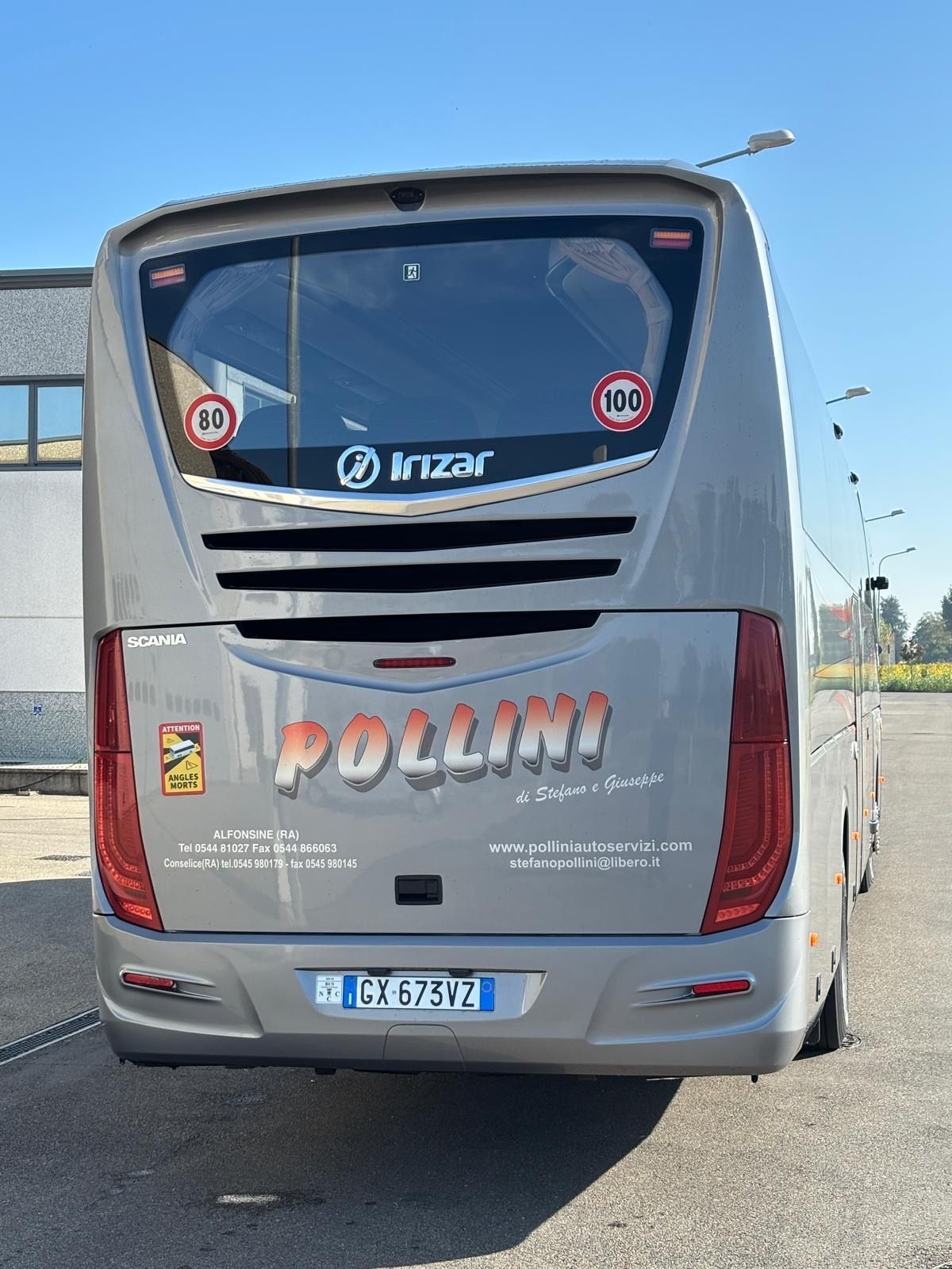 Rear view of a silver Pollini tourist bus with red rear lights, parked outside on a sunny day.