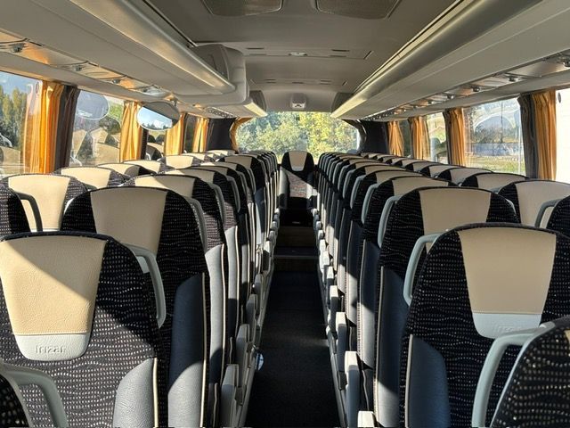 Interior view of a bus with rows of black and cream-coloured seats, windows with curtains on both sides.
