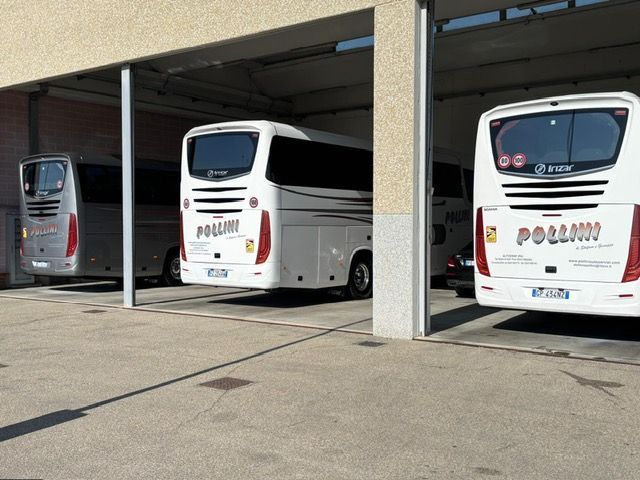 Three white buses parked under a covered structure. Each bus has the word 