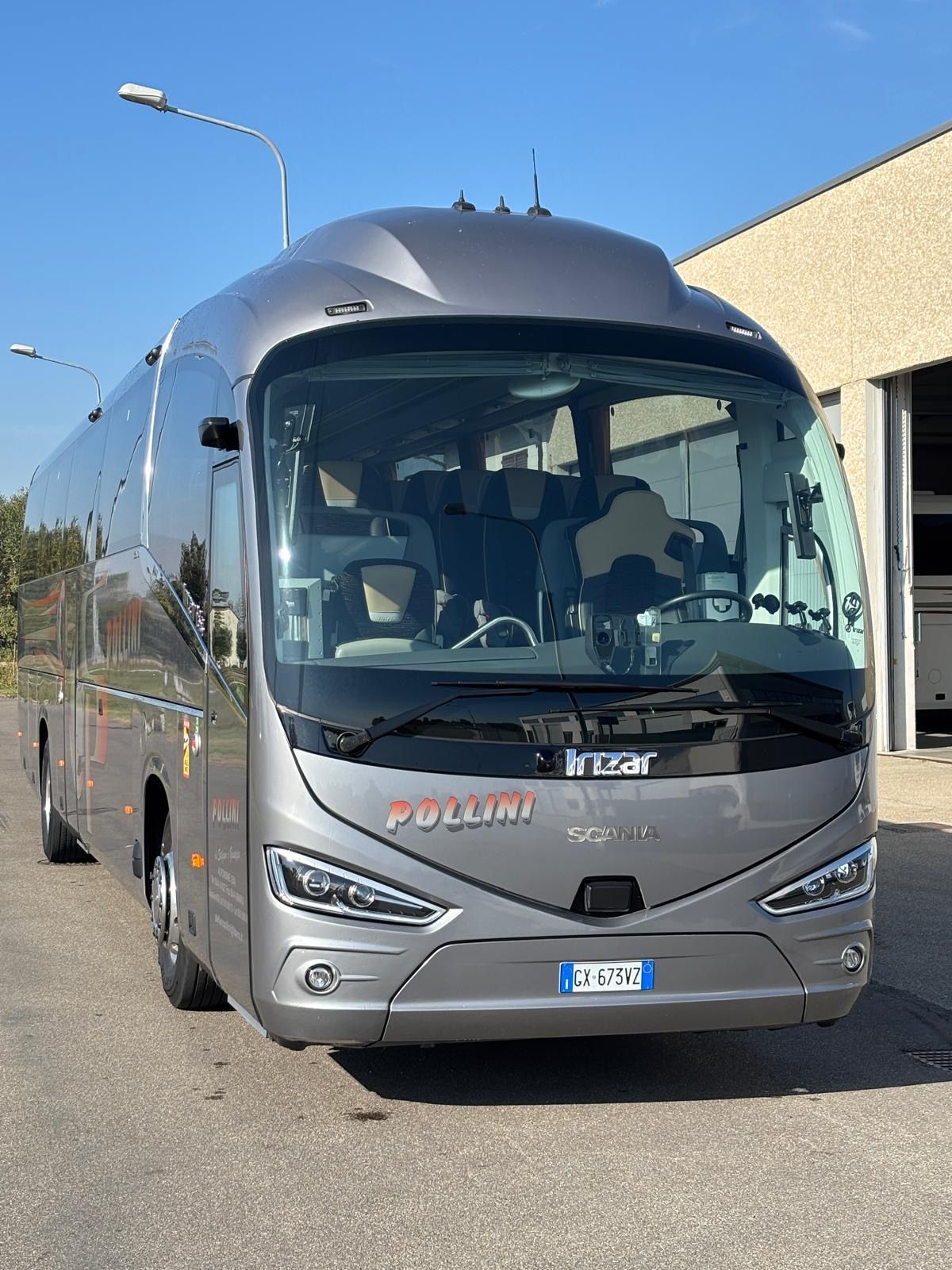 A grey tourist bus parked in front of a building on a sunny day.