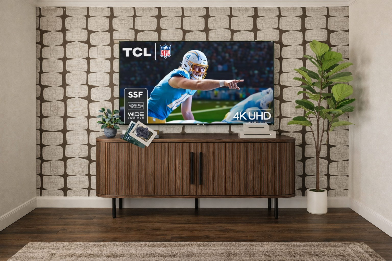 TCL TV displaying football game, sitting on a wooden cabinet, against patterned wallpaper.