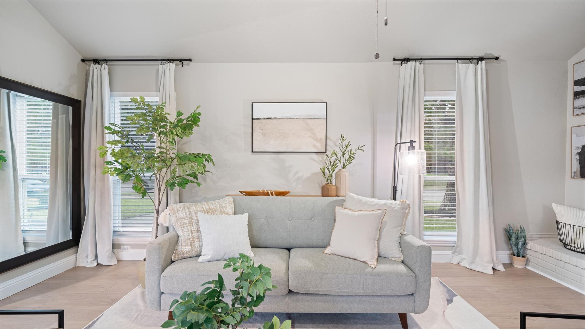 Living room with gray sofa, large mirror, windows, neutral colors, and decor.
