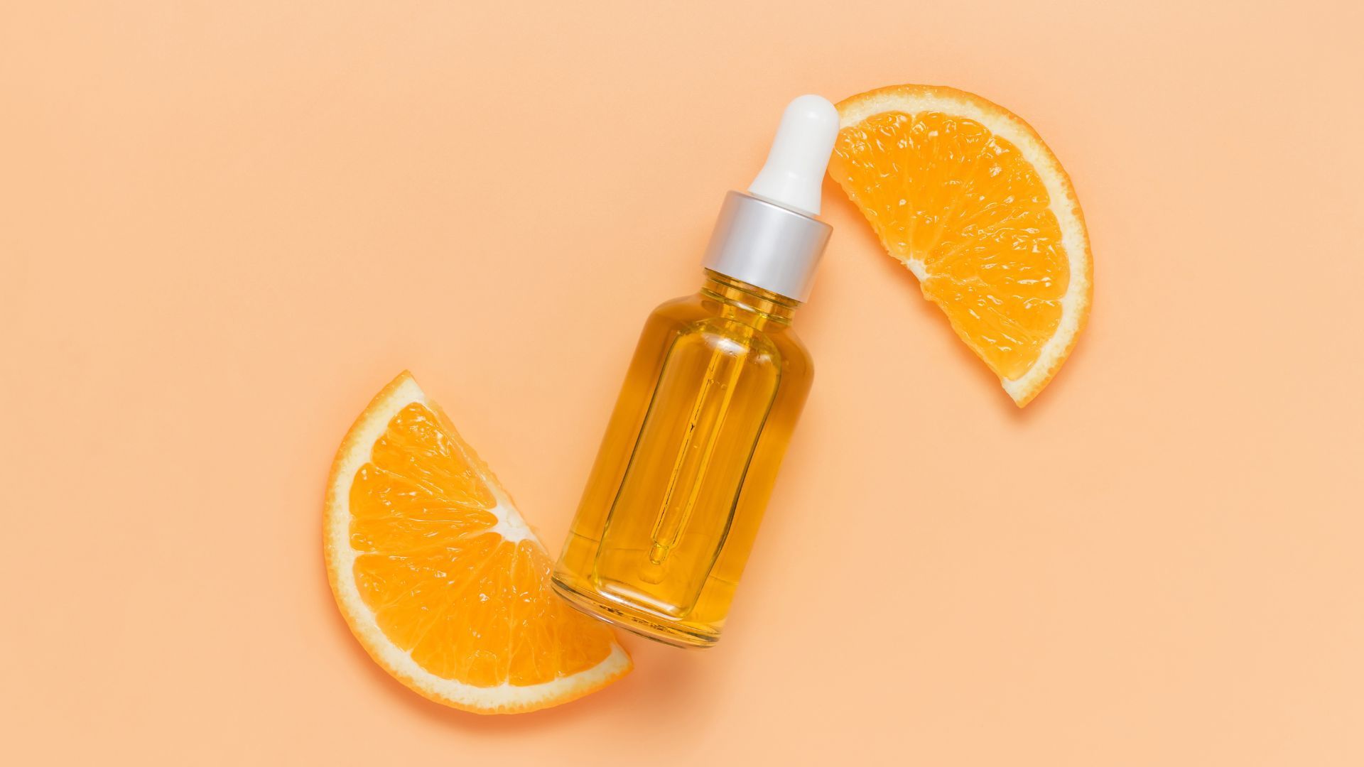 A bottle of vitamin c serum next to a slice of orange.