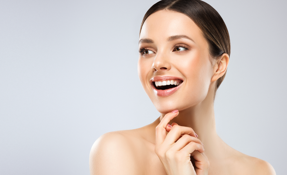 The woman is smiling and touching her face with her hand.