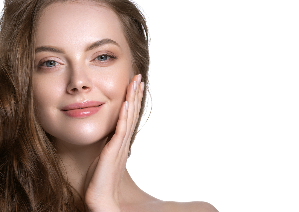 A woman is touching her face with her hand and smiling.