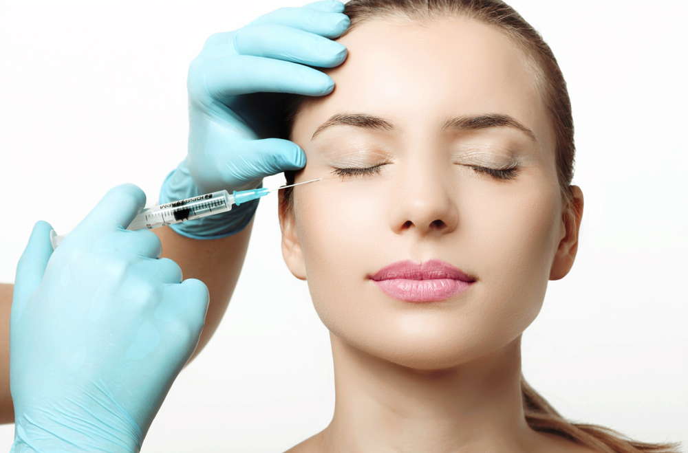 A woman is getting a botox injection in her forehead.