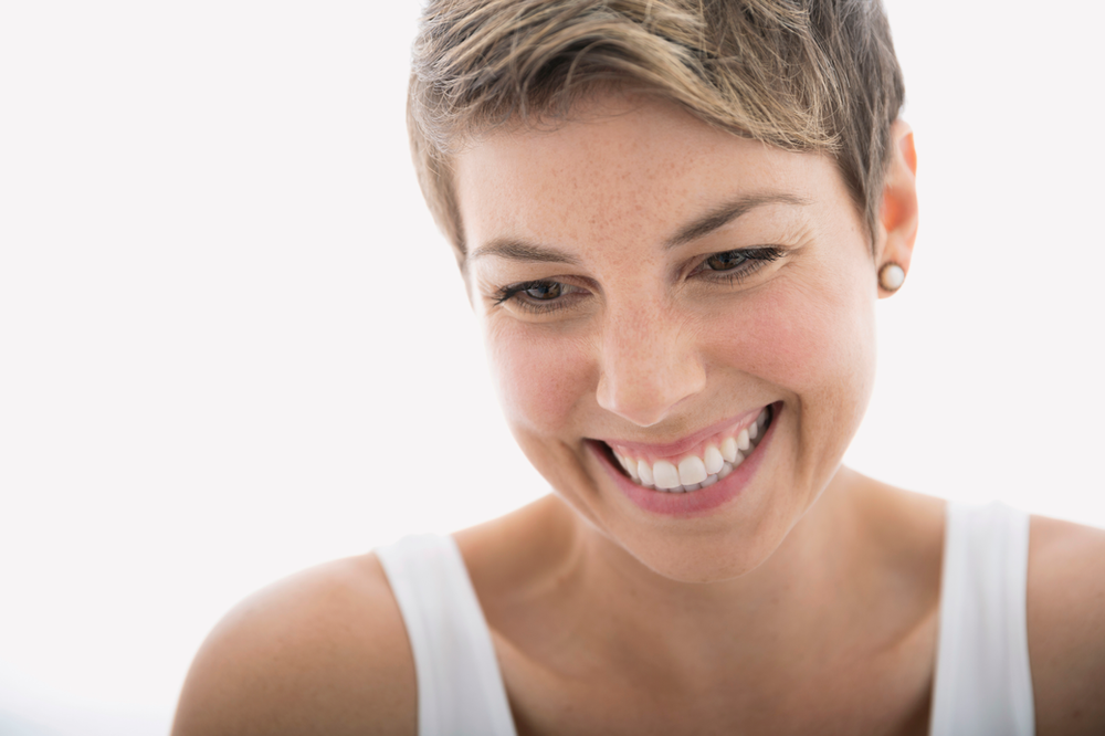 A woman with short hair is smiling and looking down.
