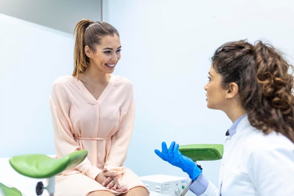 Woman smiling, talking to a doctor in an exam room. Doctor wears gloves and white coat.
