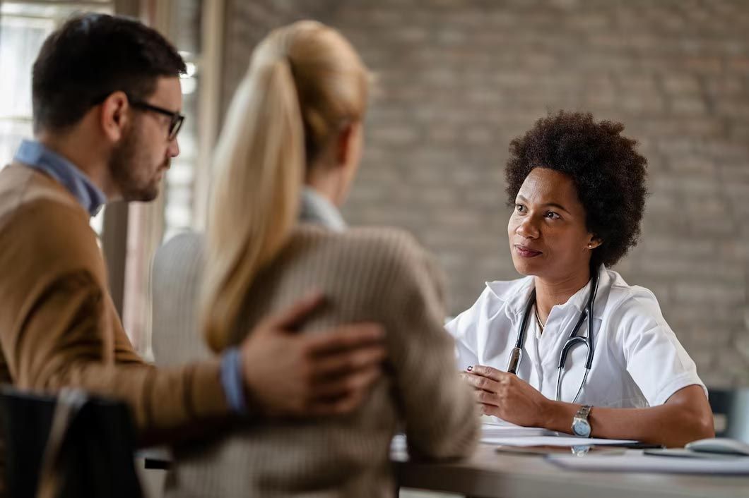 Couple consulting a doctor, listening intently. The doctor is Black, wearing a stethoscope.