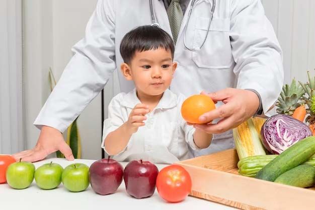 A doctor showing a young boy an orange amidst a table of colorful fruits and vegetables.