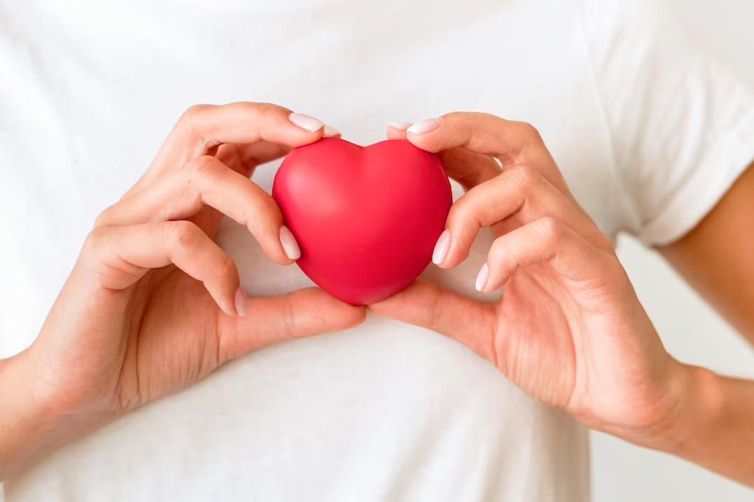 Woman holding a red heart with both hands against her chest.