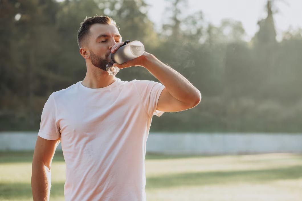 Man drinking from a water bottle on a track, wearing a white shirt.