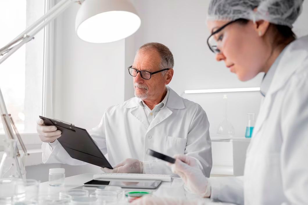 Two scientists in a lab, examining documents. One holds a clipboard, the other a magnifying glass.