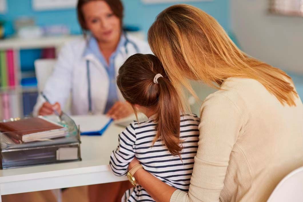 Mother comforting a child at doctor's office, doctor in background.